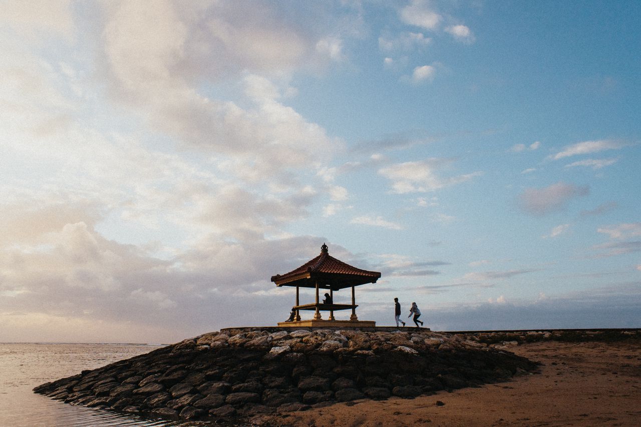 A tiled-roof pavilion on a stone breakwater beside the beach