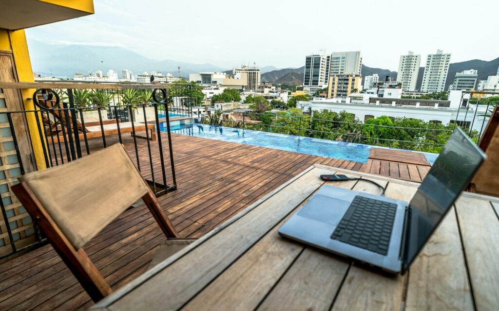 Laptop on a rooftop terrace beside a pool overlooking a city.
