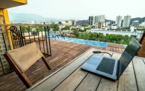 Laptop on a rooftop terrace beside a pool overlooking a city.